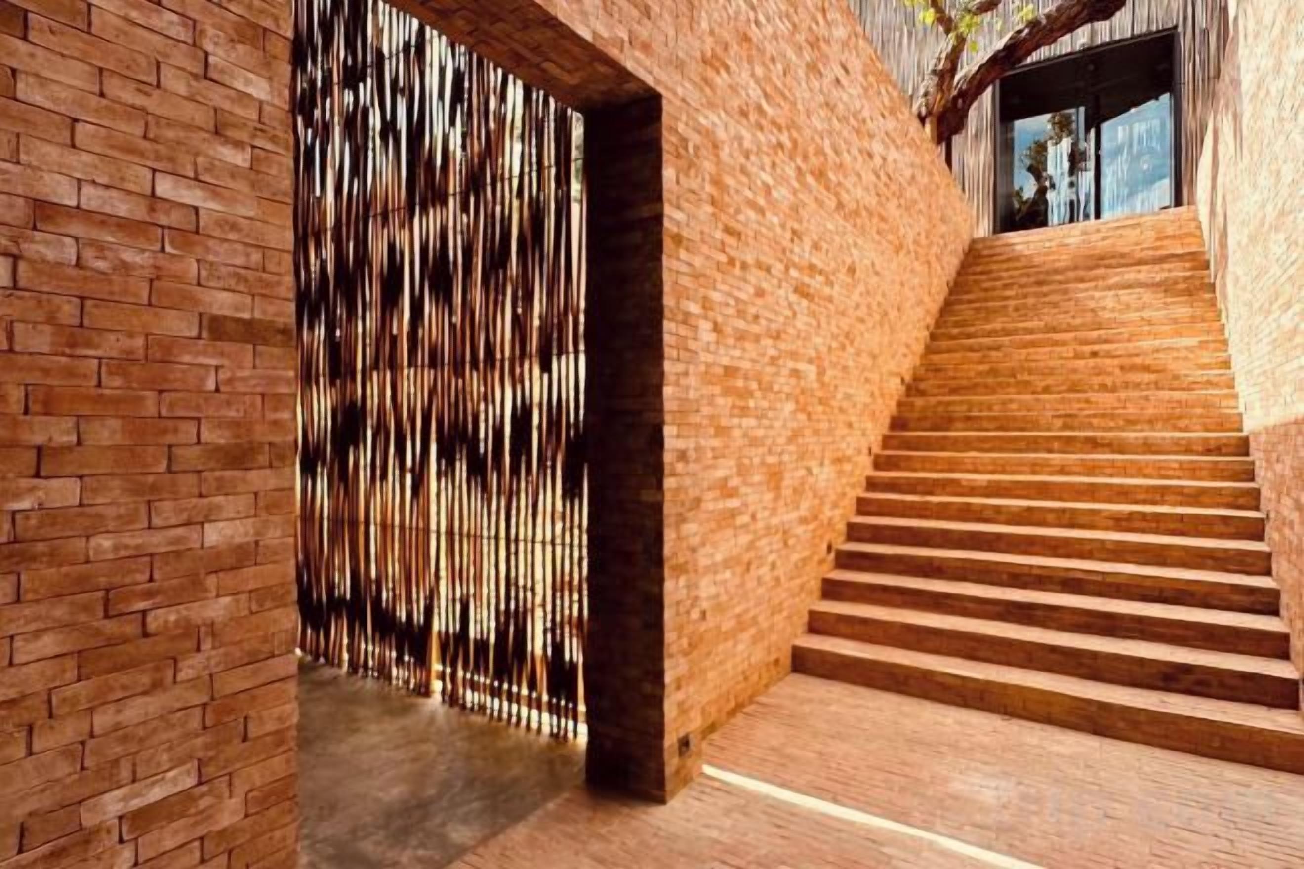 A staircase with a brick wall and a wooden floor leading to a door with vertical slats.