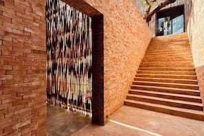 A staircase with a brick wall and a wooden floor leading to a door with vertical slats. - Historykan Kanchanaburi Hotel (Kanchanaburi)