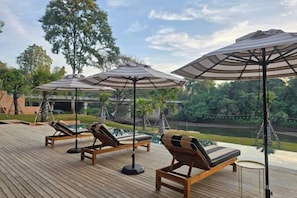 A deck with lounge chairs and umbrellas, overlooking a body of water and greenery. - Historykan Kanchanaburi Hotel (Kanchanaburi)