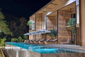 A modern outdoor pool area with lounge chairs and umbrellas, surrounded by bamboo walls and greenery. - Historykan Kanchanaburi Hotel (Kanchanaburi)