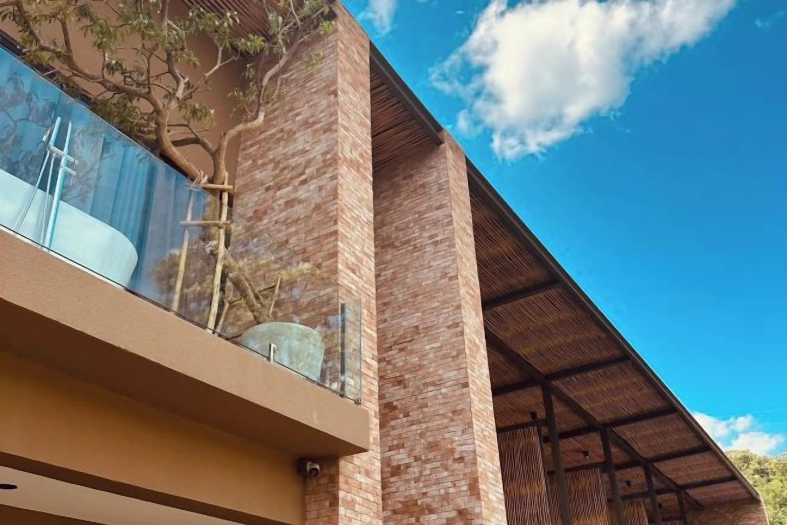 A modern building with a glass balcony, brick walls, and a clear blue sky.