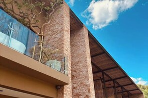 A modern building with a glass balcony, brick walls, and a clear blue sky. - Historykan Kanchanaburi Hotel (Kanchanaburi)