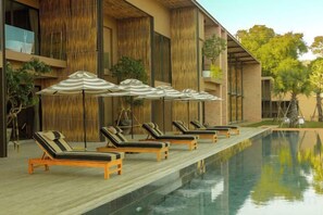 A poolside area with lounge chairs and umbrellas, a wooden deck, and a building with vertical wooden slats. - Historykan Kanchanaburi Hotel (Kanchanaburi)