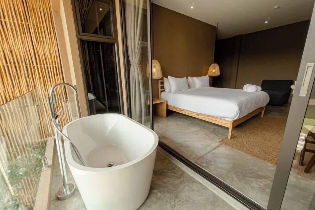 Una habitación de hotel moderna con una bañera grande, una cama y una mesita de noche.