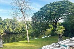 A serene outdoor setting with a grassy area, a tree, and a body of water. - Historykan Kanchanaburi Hotel (Kanchanaburi)
