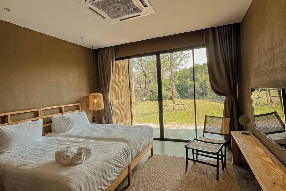 Un dormitorio con una cama grande, un escritorio y una silla. Se ve un jardín a través de la ventana.