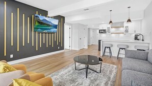 Ein modernes Wohnzimmer mit Flachbildfernseher, rundem Couchtisch und grauem Sofa.