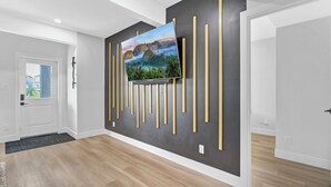 Ein modernes Interieur mit einem Wand-Fernseher an einer dunklen Wand, Holzboden und einer Tür, die zu einem Außenbereich führt.