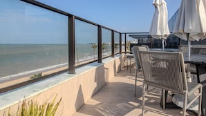 A balcony with a view of the ocean, outdoor seating, and umbrellas. - CSQ Jardins  (João Pessoa)