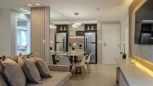 A modern kitchen with built-in appliances, a dining area with a glass table and chairs, and a living area with a sofa and cushions. - CSQ Jardins  (João Pessoa)