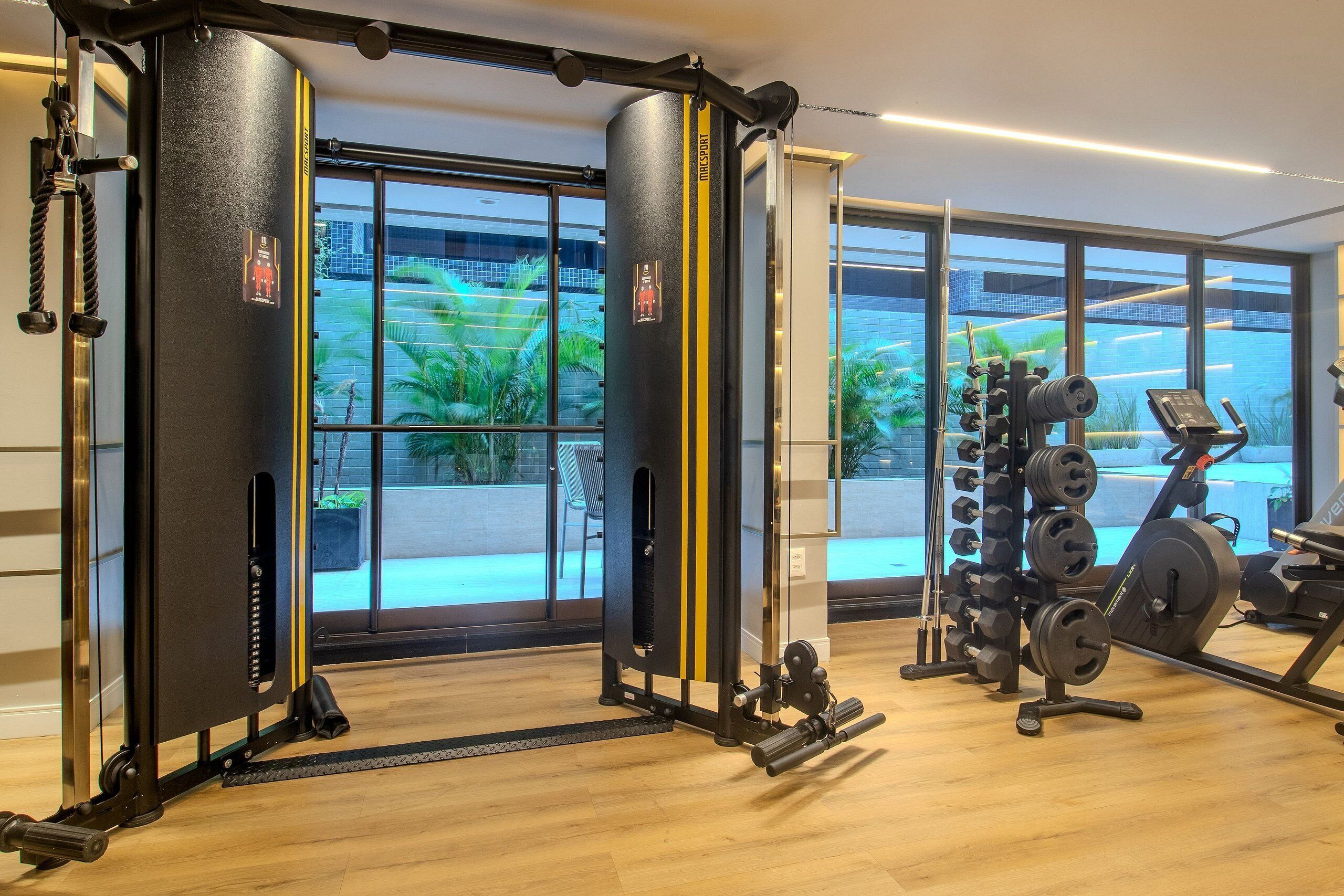 Et fitnesscenter med styrkeløftningsudstyr, store vinduer og udsigt til grøn natur.