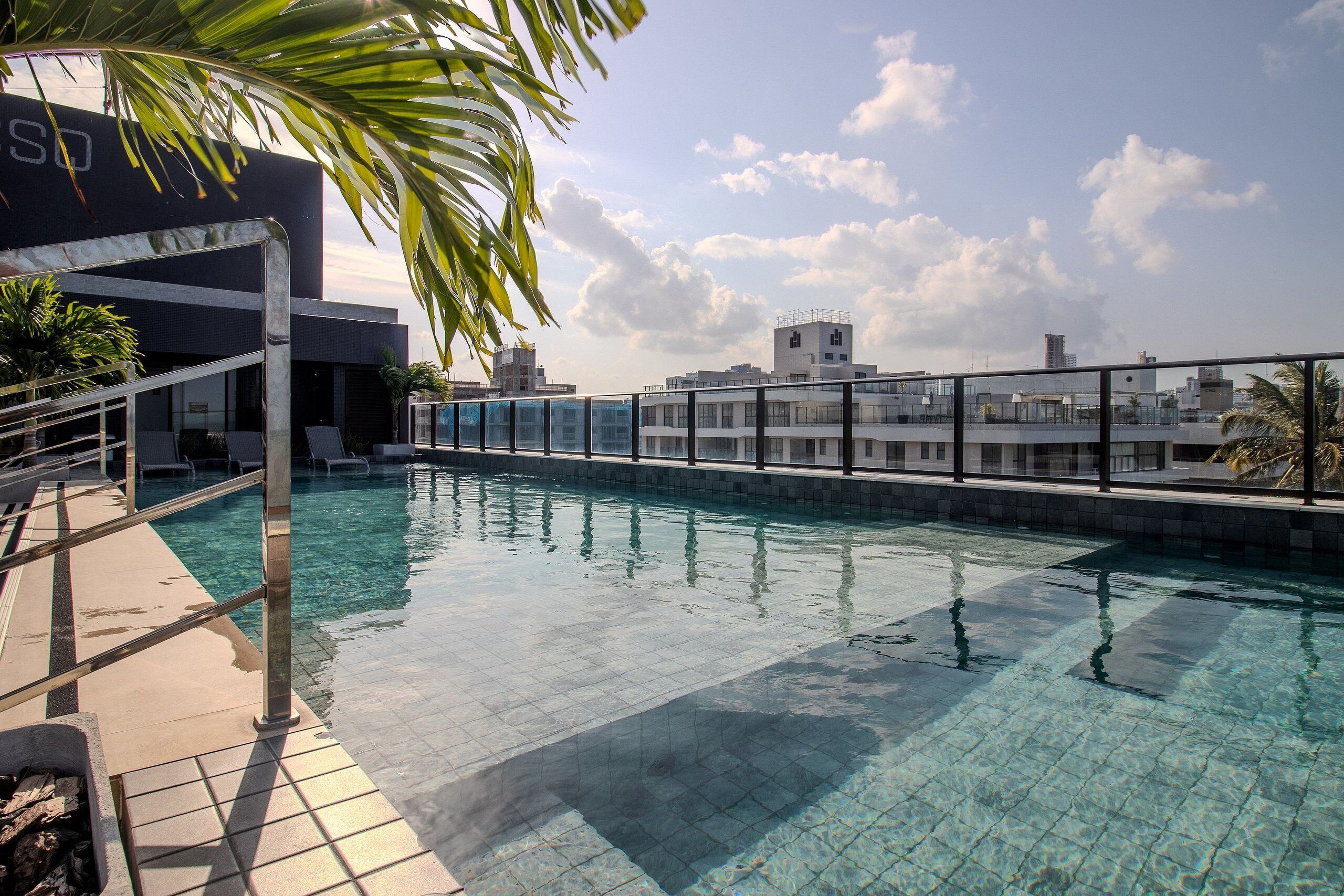 A swimming pool with a clear blue water surface, surrounded by a tiled deck and a glass barrier.