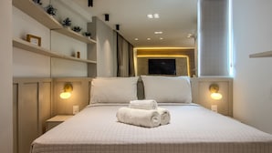 A neatly made bed with a quilted bedspread, two bedside lamps, and a flat-screen TV mounted on the wall. - CSQ Jardins  (João Pessoa)