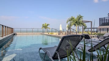 Une piscine sur le toit, avec des chaises longues, des palmiers et une vue sur la mer.