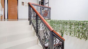 A staircase with a black railing and white steps, leading to a landing with a wooden door and framed pictures on the wall. - Hotel O Rumah Daun Guesthouse Jogja (Yogyakarta)