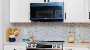 A kitchen with white cabinets, a black microwave, a stove, and a tiled backsplash. - Fantastic 4-bedroom Home on Lake Bowen (Inman)