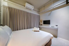 Een hotelkamer met een bed, een televisie op een standaard, een gordijn en een airconditioner.