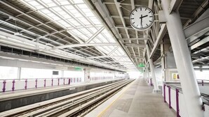 A train station platform with a clock, tracks, and overhead structure.