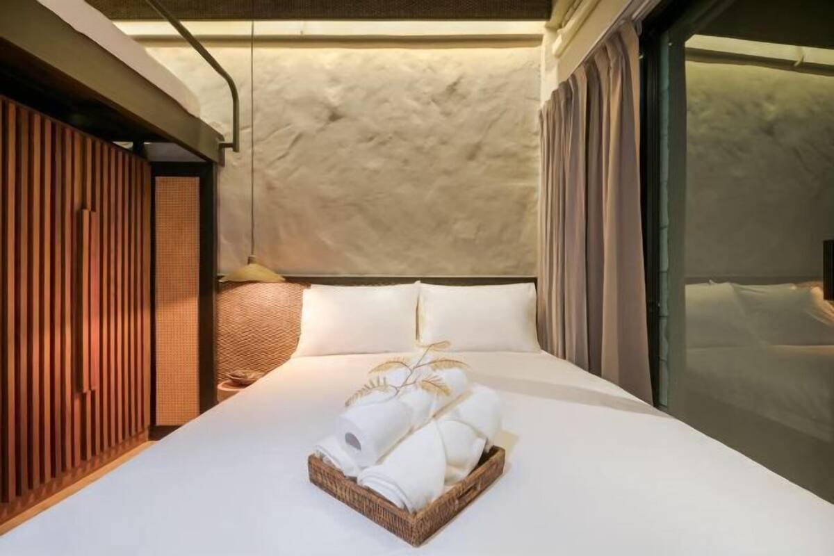 Ein Hotelzimmer mit Bett, einer Holzwand, einem Nachttisch und einem Fenster mit Vorhängen.