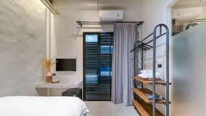 A modern hotel room with a bed, a desk, a TV, a wardrobe with shelves, and an air conditioning unit.
