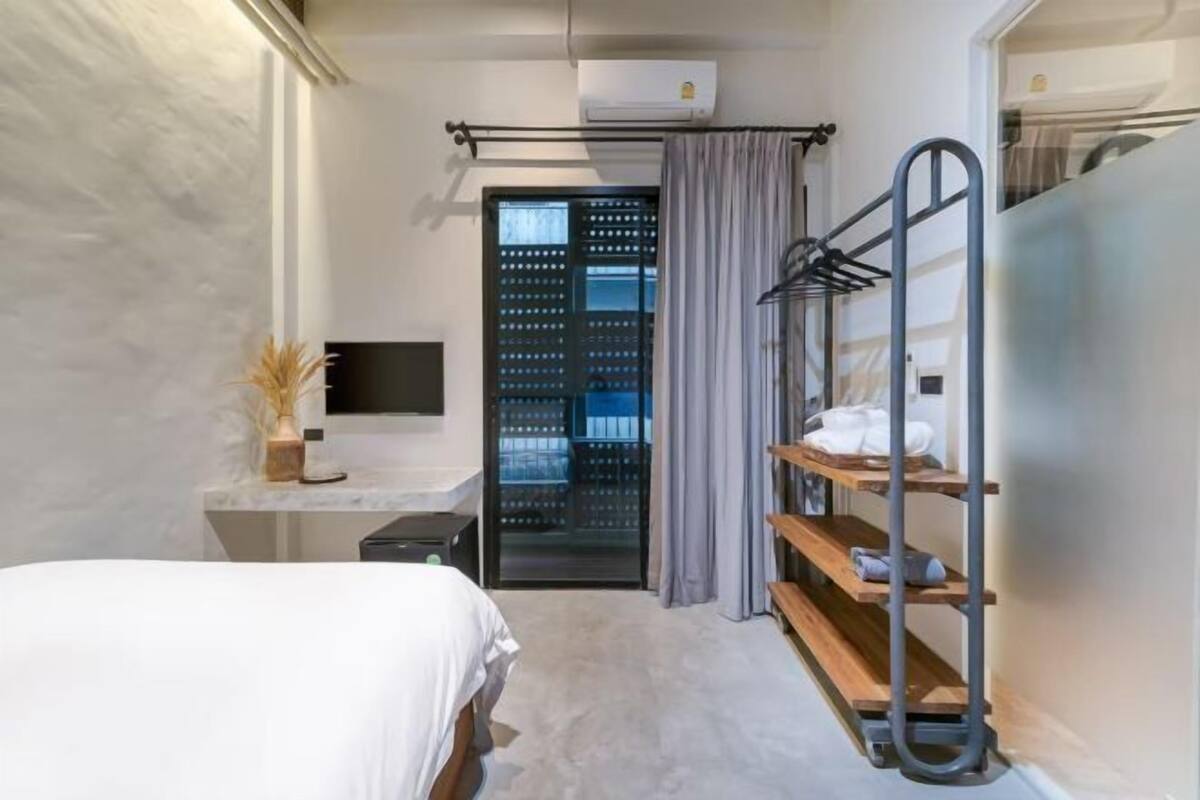 Ein modernes Hotelzimmer mit Bett, Schreibtisch, Fernseher, Kleiderschrank mit Regalen und einer Klimaanlage.