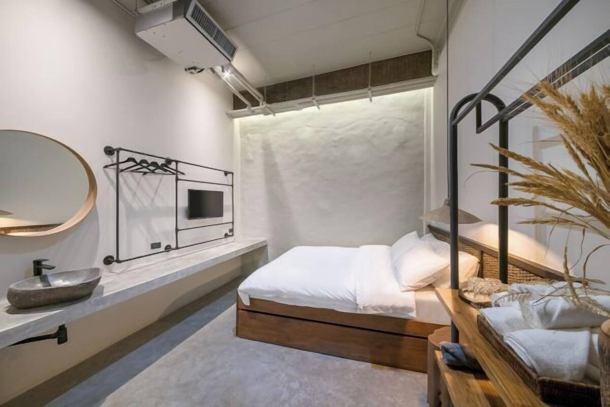 Ein modernes Schlafzimmer mit einem hölzernen Bett, einem runden Spiegel, einem Nachttisch mit einer Schale und einer wandmontierten Leuchte.
