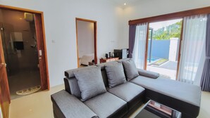Een moderne woonkamer met een grijze modulaire bank, een salontafel en een televisie. Er is een schuifdeur naar een balkon met uitzicht op een zwembad.
