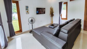 Een moderne woonkamer met een grijze modulaire bank, een flatscreen televisie, een ventilator en een vaas met gedroogde planten.