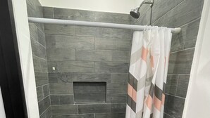 A shower area with dark stone tiles, a showerhead, and a curtain. - Lavish Studio w Kitchen Downtown 1 (Isla Mujeres)
