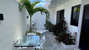 A narrow outdoor corridor with a glass table and chairs, surrounded by white walls and potted plants. - Lavish Studio w Kitchen Downtown 1 (Isla Mujeres)