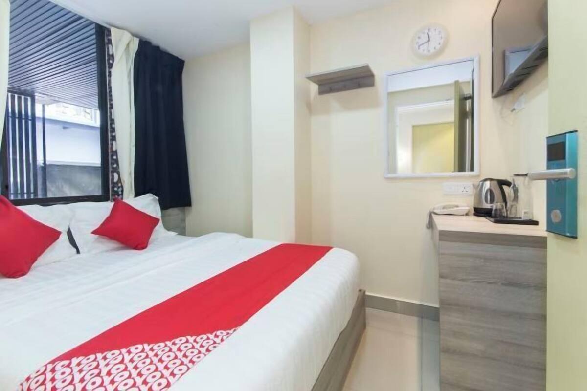 Hotelkamer met een bed, nachtkastje, spiegel, klok en raam met gordijnen.