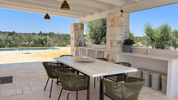 Une terrasse extérieure avec une table et des chaises en pierre, une piscine et un mur en pierre.