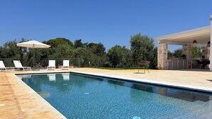 Une piscine à l’eau claire, entourée de chaises longues et de parasols.