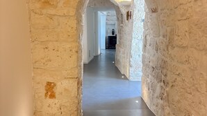 Un couloir aux murs de pierre et au plancher en bois, qui mène à une pièce dotée d’une porte blanche.