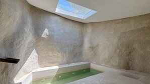Une salle de spa dotée d’une verrière, d’un élément décoratif aquatique aux eaux verdoyantes et d’un mur en pierre.