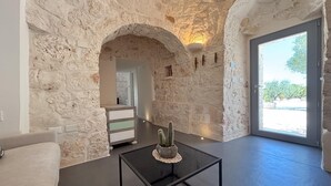 Une pièce aux murs de pierre, avec une table basse en verre et une porte donnant sur l’extérieur.