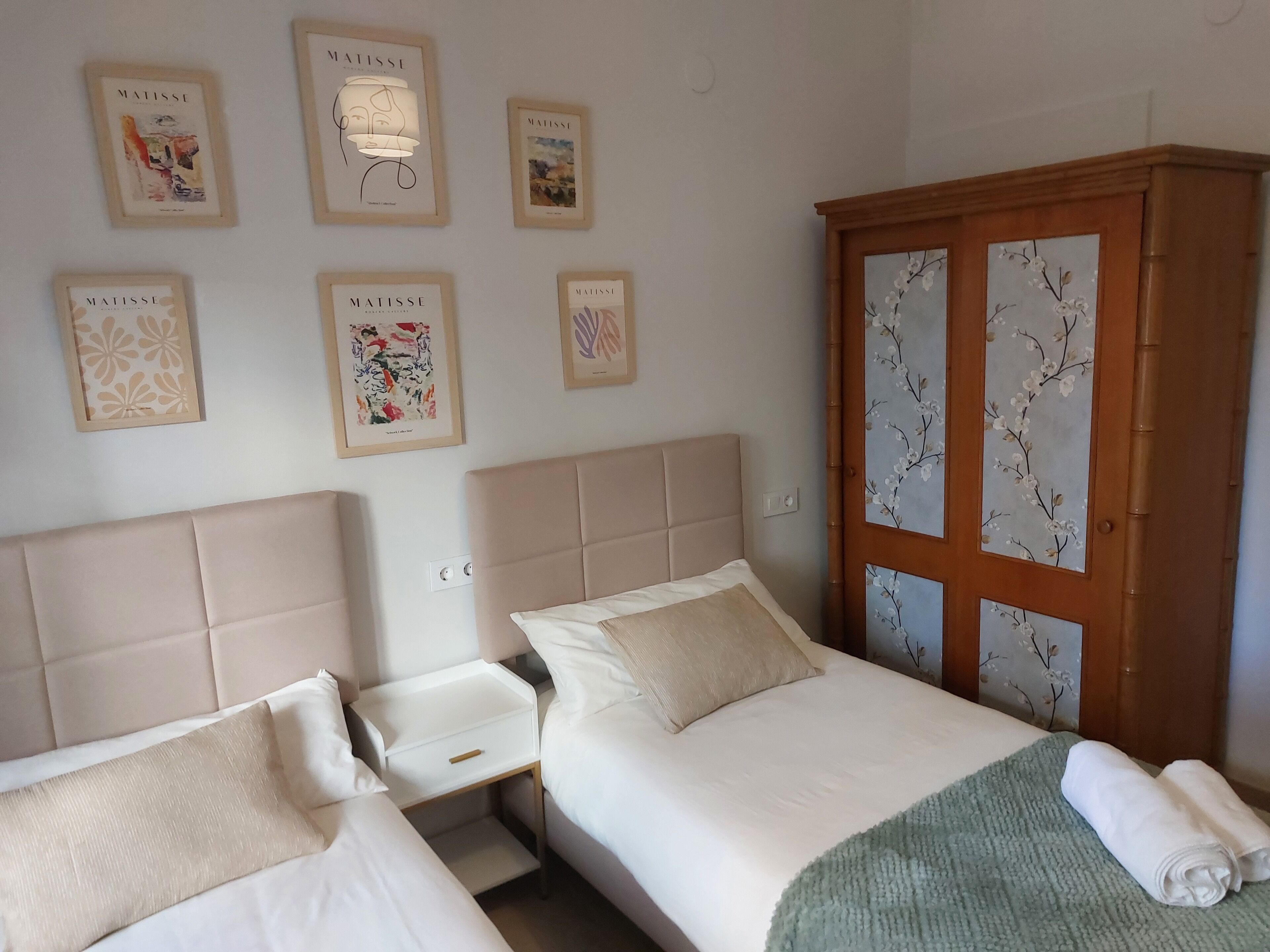 Een hotelkamer met twee bedden, een houten garderobe en kunstwerken in een lijst aan de muur.