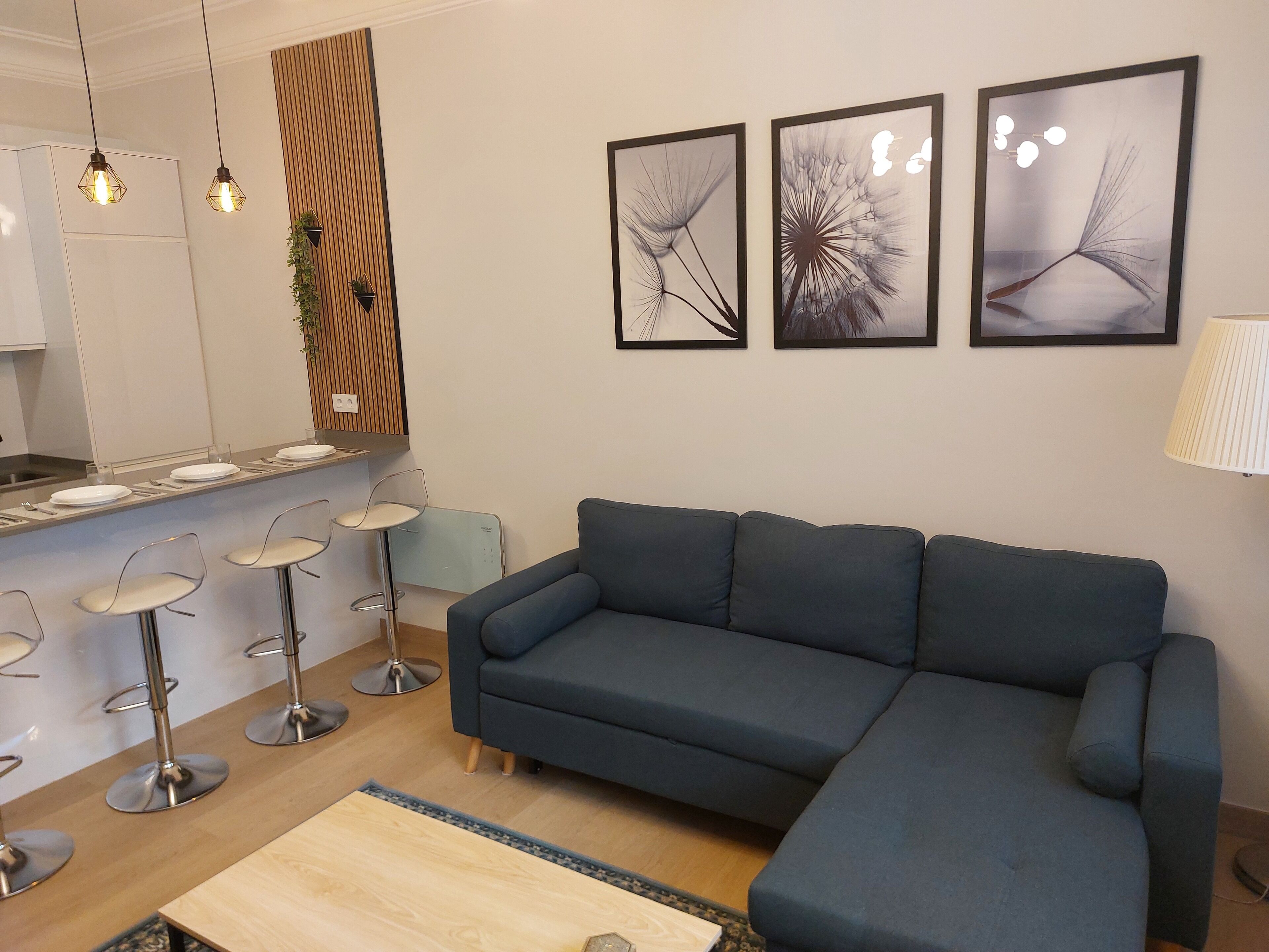 Una sala de estar moderna con un sofá modular, un comedor con taburetes de bar y tres cuadros en la pared.