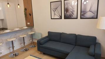 Una sala de estar moderna con un sofá modular, un comedor con taburetes de bar y tres cuadros en la pared.