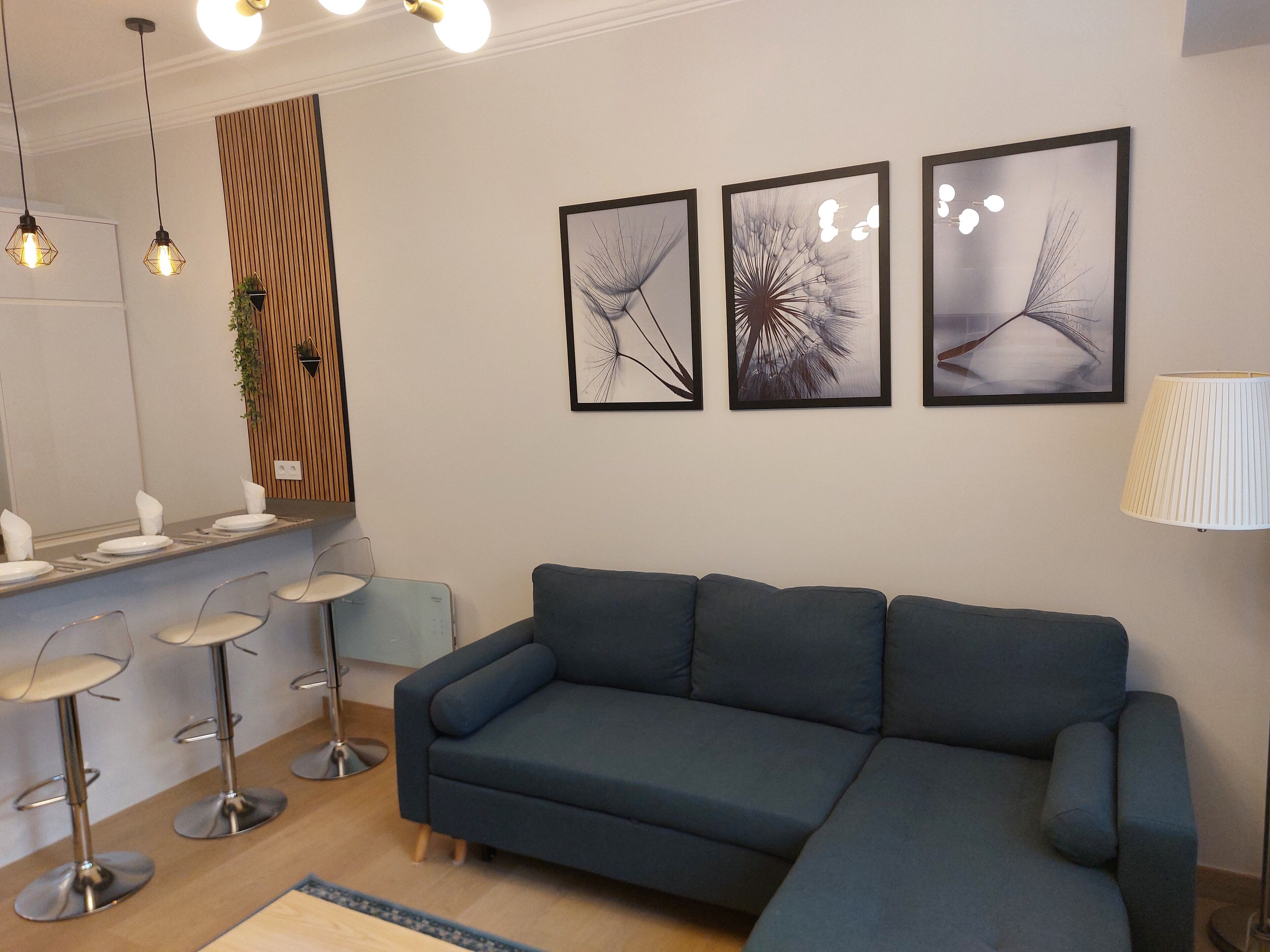 A modern living room with a blue sectional sofa, a dining area with a bar stool, and three framed abstract wall art pieces.