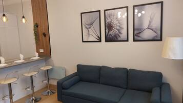 A modern living room with a blue sectional sofa, a dining area with a bar stool, and three framed abstract wall art pieces.