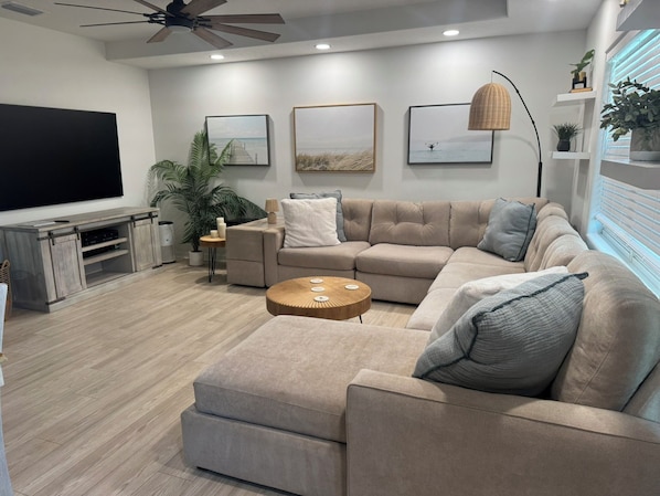 A modern living room with a sectional sofa, a coffee table, a TV, and artwork on the walls. - A Fancy Flamingo Historic Downtown Melbourne 5 minute drive Beaches and Airport (Melbourne)