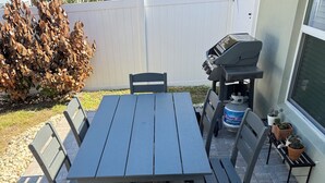 Un patio con mesa y sillas, una parrilla y plantas en macetas.