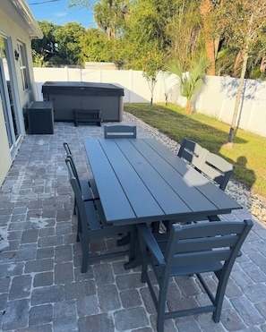 An outdoor patio with a dark wooden table and benches, surrounded by a stone floor and a white fence. - A Fancy Flamingo Historic Downtown Melbourne 5 minute drive Beaches and Airport (Melbourne)