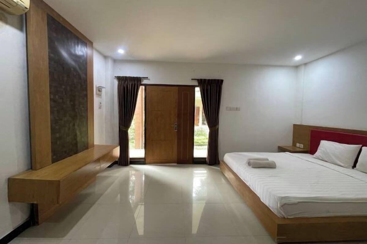 A hotel room with a bed, a bench, a wooden door, and a view through the door.