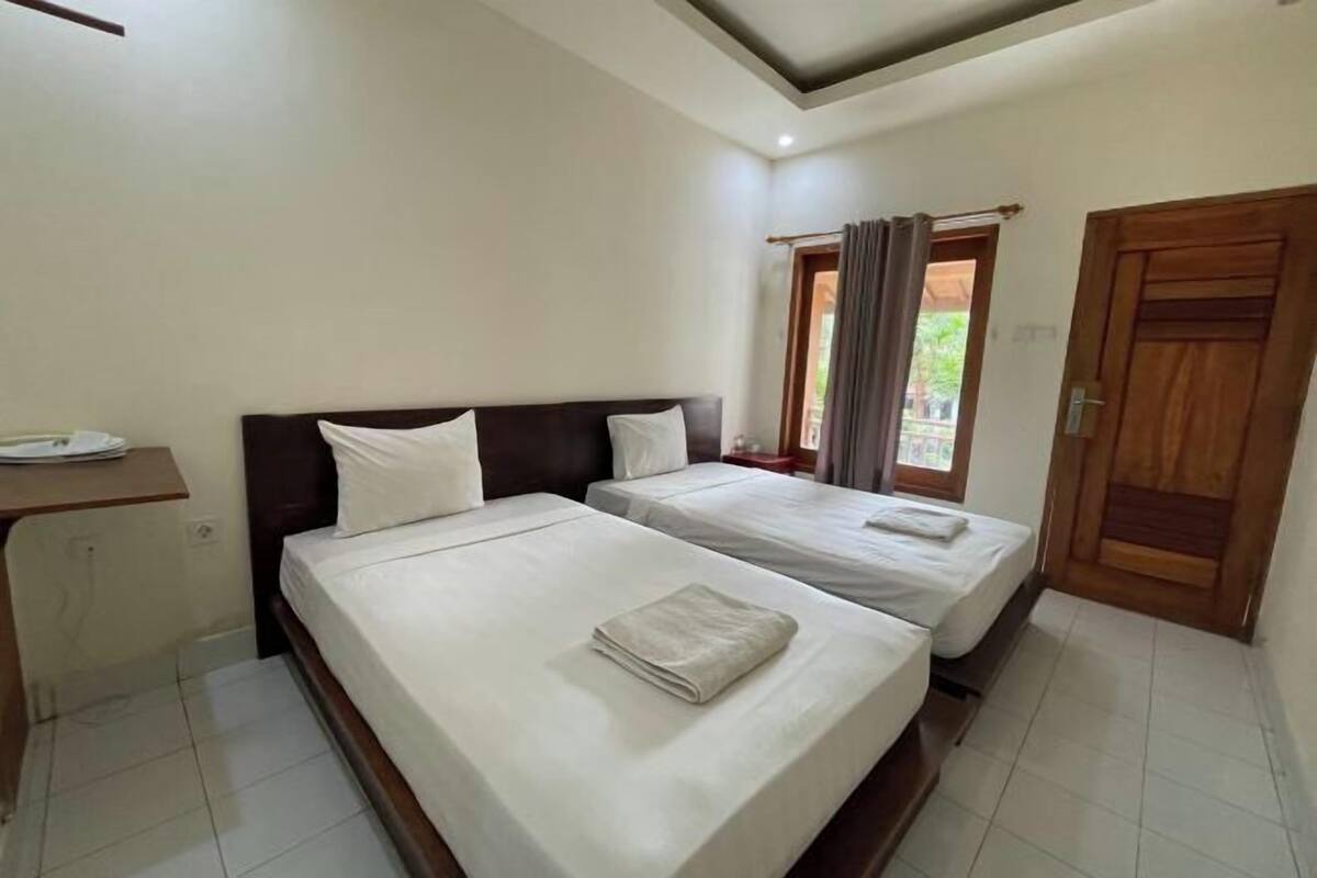 A hotel room with two beds, a wooden headboard, a small desk, and a door.