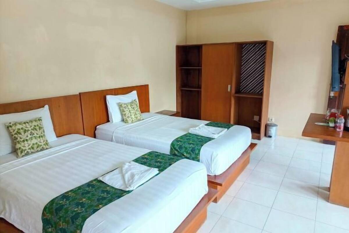 A hotel room with two beds, a wardrobe, a small table with items, and a trash bin.