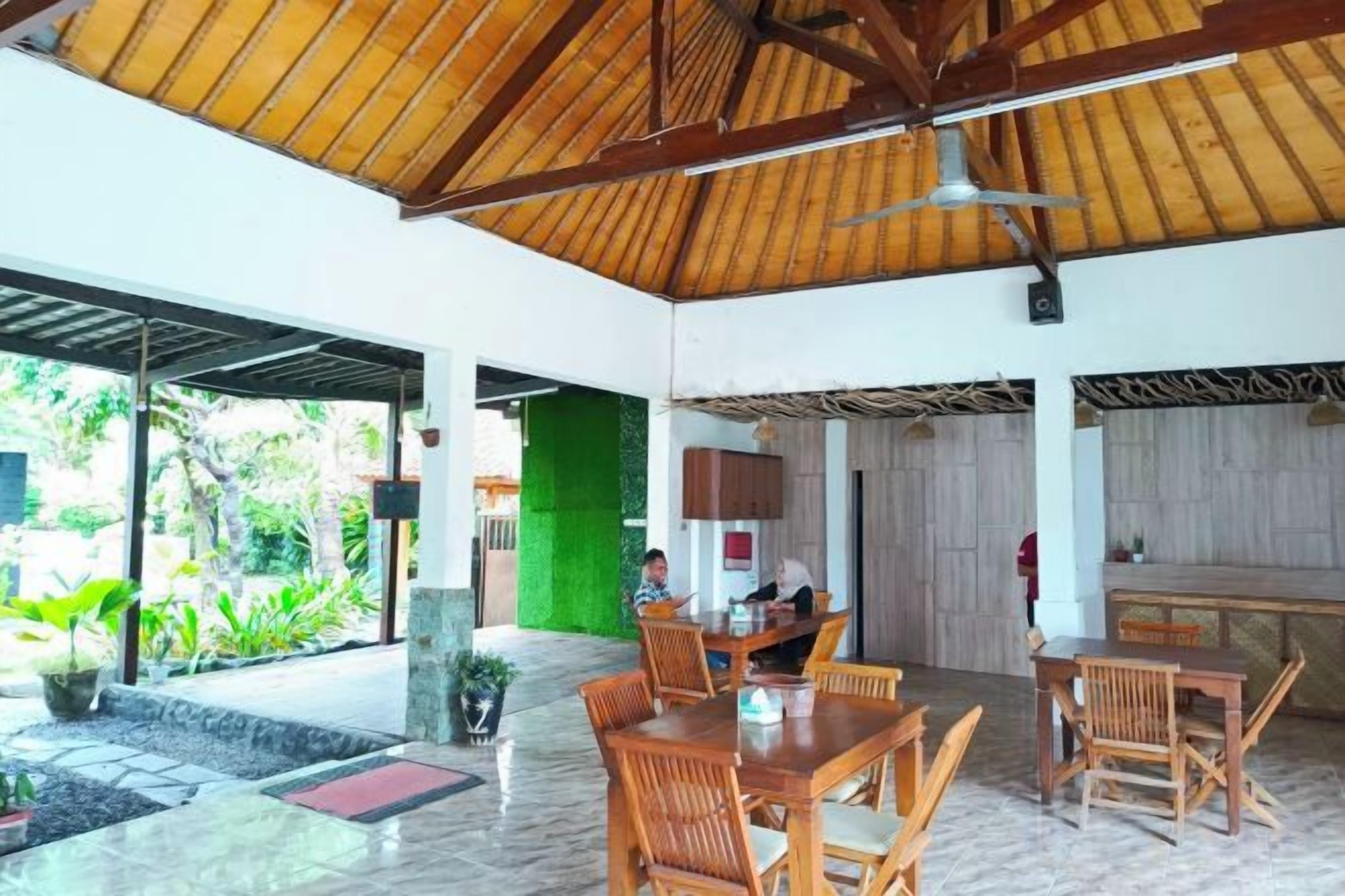 An indoor dining area with wooden tables and chairs, a ceiling fan, and a view of the outdoors.