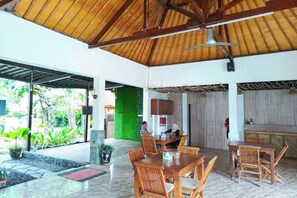 Un comedor interior con mesas y sillas de madera, un ventilador de techo y vistas al exterior.