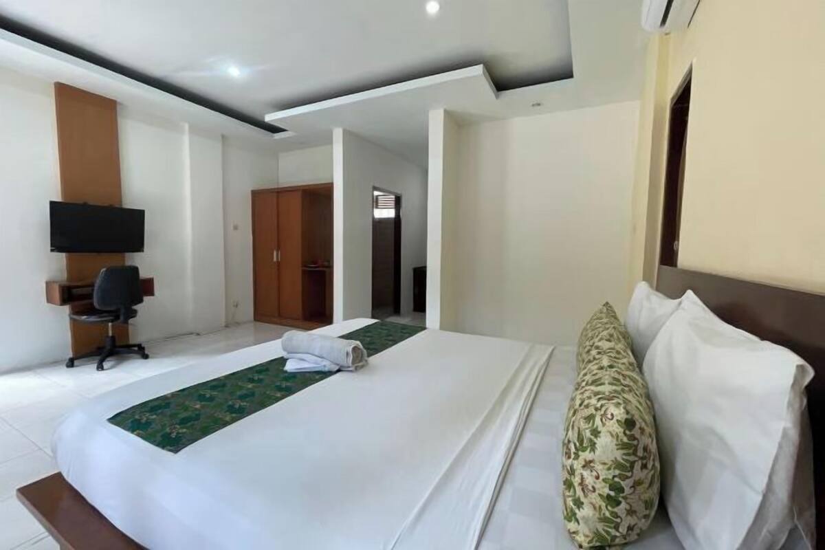 A hotel room with a bed, a desk, a chair, a TV, and a wardrobe.